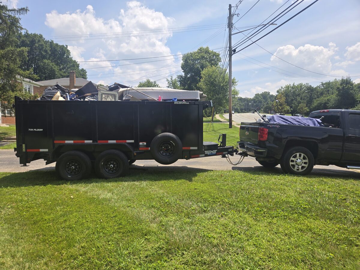 The NYA Junk Removal pickup and high-wall dump trailer parked at the curb on a residential street.