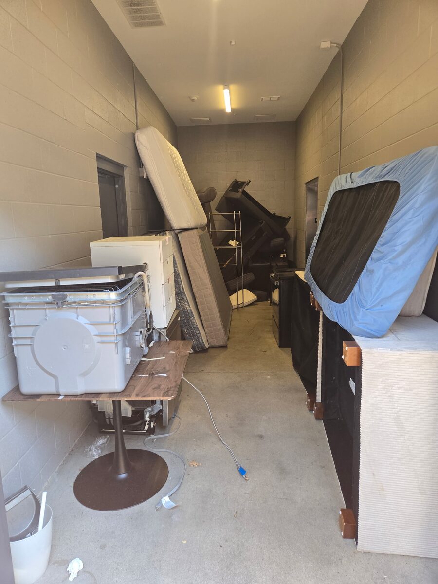 A storage corridor stacked with mattresses, a mini fridge, storage totes and tenant leave-behinds waiting for removal.