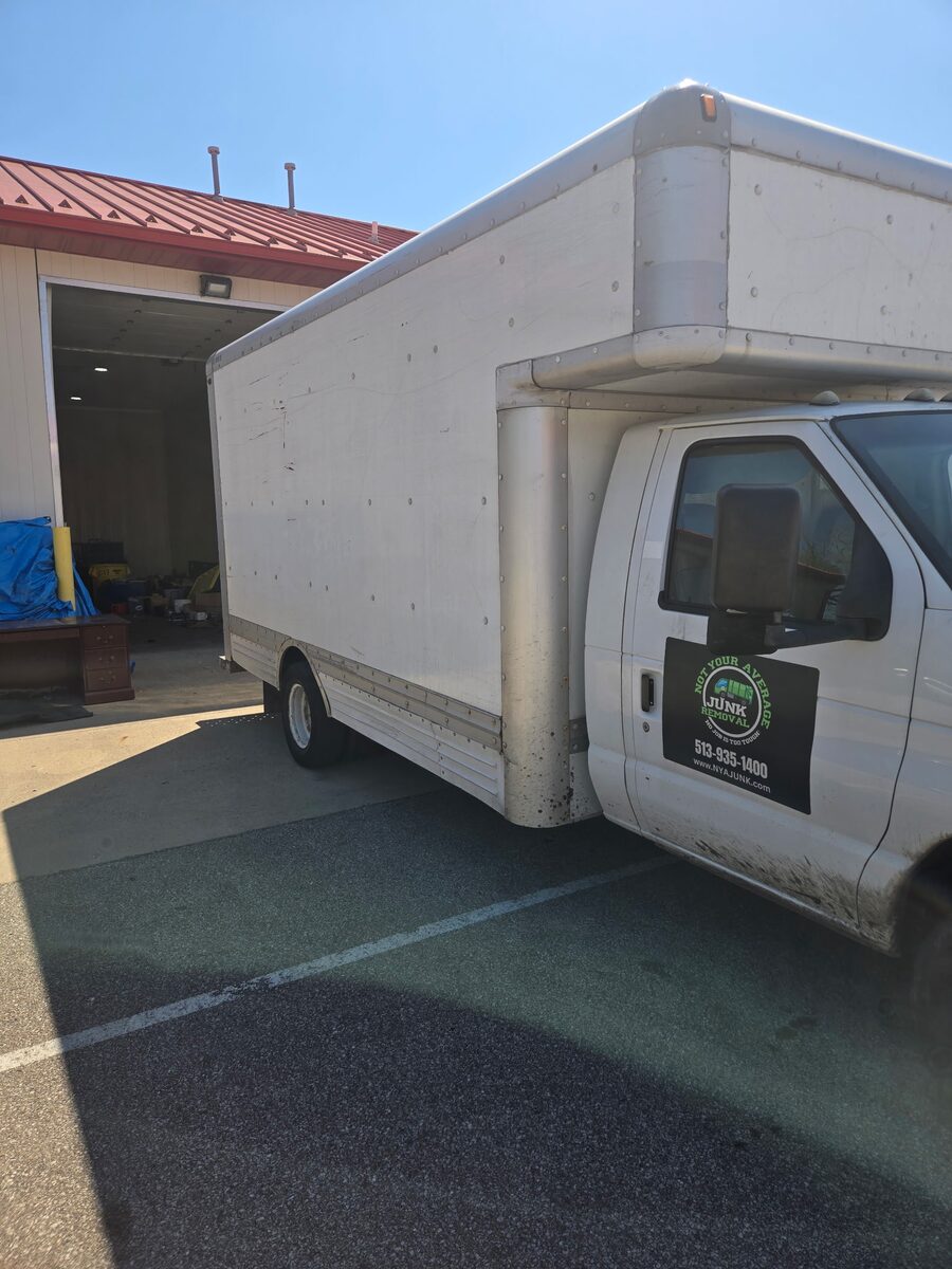 The NYA Junk Removal 15-foot white box truck with the company logo and phone number on the cab door, parked outside the shop.