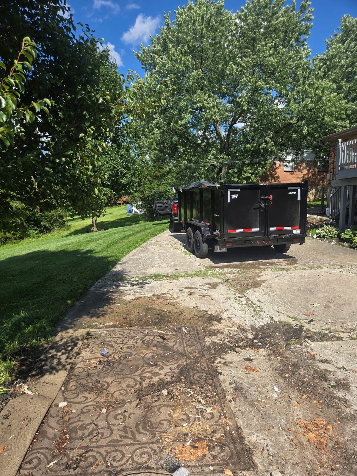 NYA Junk Removal’s black high-wall dump trailer backed up a residential driveway, ready to load.